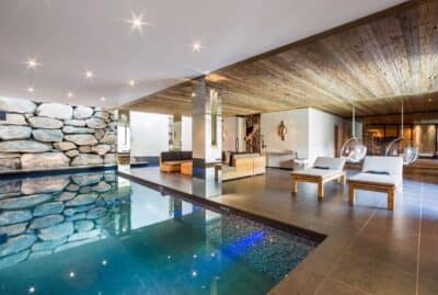 chalet-norte-indoor-swimming-pool-and-spa-area Luxurious indoor pool area with stone accent wall, wooden ceiling, modern lounge chairs, and a seating area, all in a spacious, well-lit room with contemporary decor. David Pearson Travel