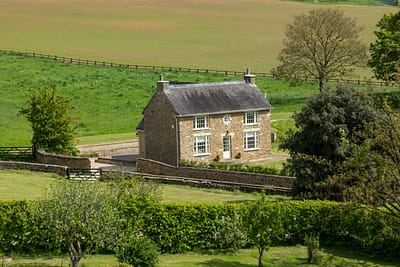 Javelin 1 A stone cottage with a slate roof sits in a lush, green countryside surrounded by trees, hedges, and fields under a clear sky. The setting is peaceful and rural. David Pearson Travel