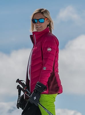 Screenshot 2026-04-08 at 13.48.46 A person wearing a bright pink jacket, green pants, and sunglasses stands outdoors in a snowy, mountainous area, holding ski poles and smiling. David Pearson Travel