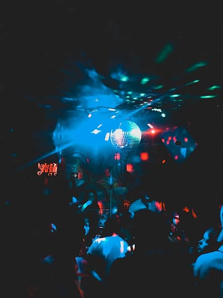 photo-1570207859654-a9a7ad65ed3d A dimly lit nightclub in Verbier with a crowd of people dancing under blue and red lights, as reflections from a disco ball create colorful patterns on the ceiling and walls—a vibrant scene for Verbier tourism. David Pearson Travel